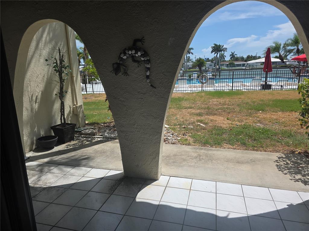 A tiled patio with arched openings overlooks a grassy yard, a swimming pool, and water — 507 PLAZA SEVILLE COURT UNIT 15, ST PETERSBURG, FL