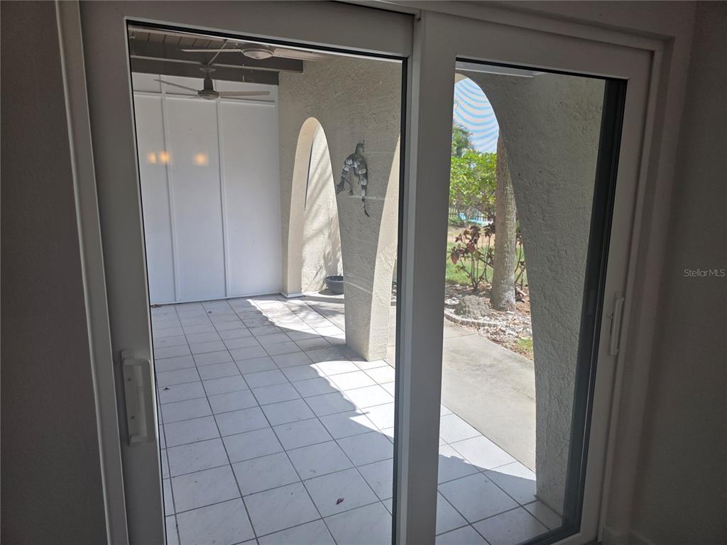 A view through sliding glass doors reveals a tiled patio with arched architectural columns — 507 PLAZA SEVILLE COURT UNIT 15, ST PETERSBURG, FL