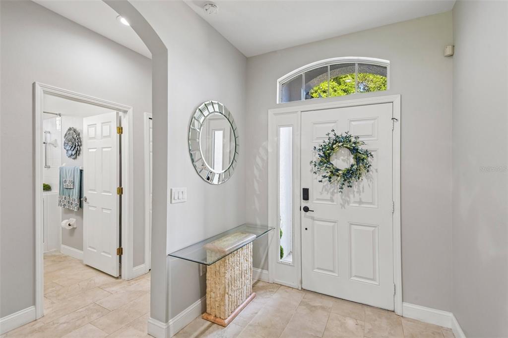 An entryway features a glass console table, a round mirror, and a white front door — 15914 CEDAR ELM TERRACE, LAND O LAKES, FL