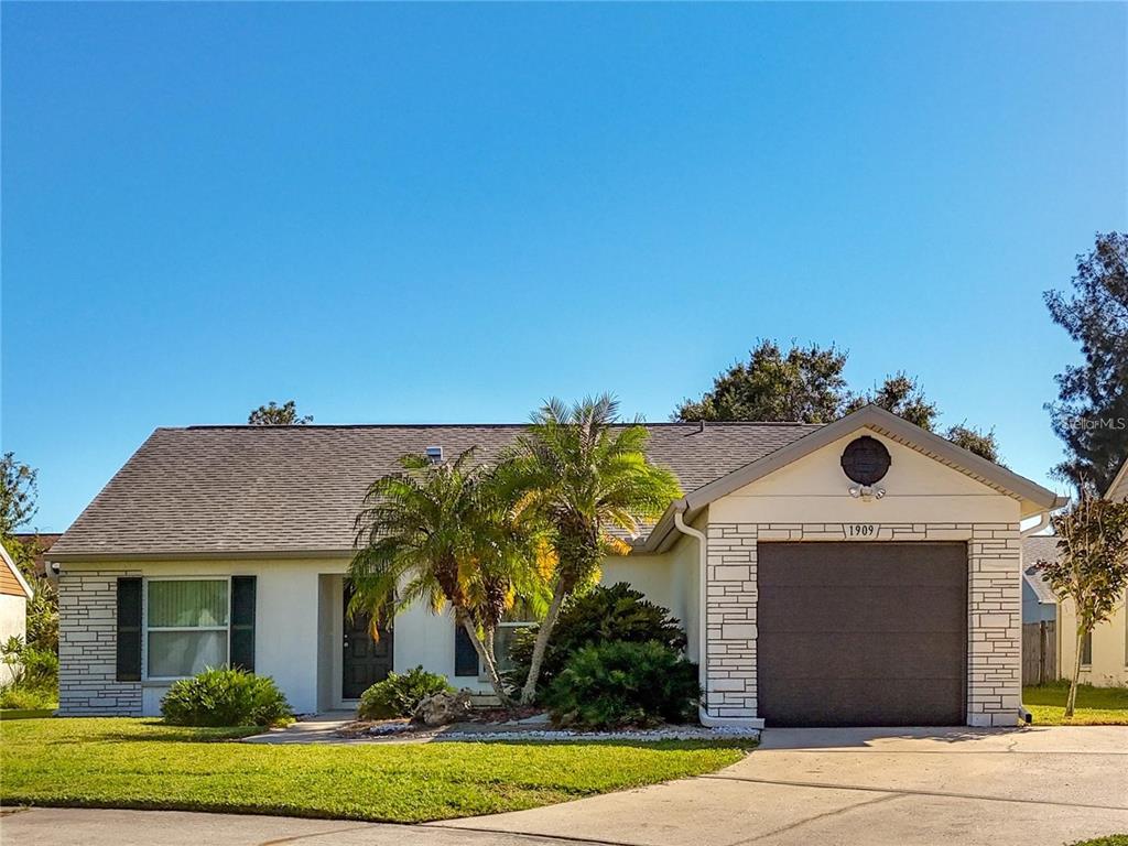 A single-story house with a white exterior, stone accents, a garage, and palm trees — 1909 CASTLE BAY COURT, OLDSMAR, FL