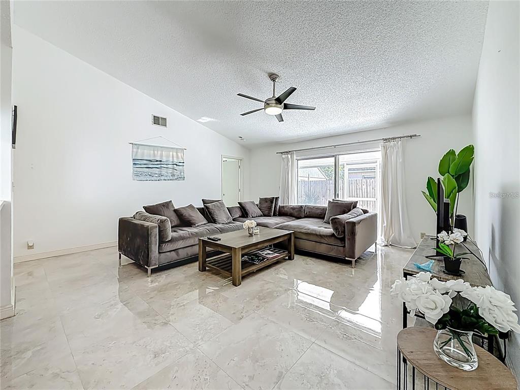 A living room features a large grey sectional sofa, a coffee table, and tile flooring — 1909 CASTLE BAY COURT, OLDSMAR, FL