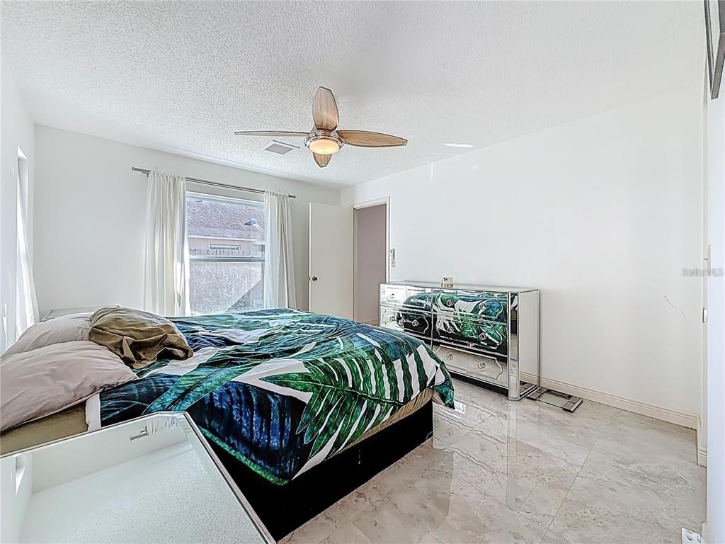 A bedroom features a palm-print comforter, mirrored dresser, ceiling fan, and light-colored tile flooring — 1909 CASTLE BAY COURT, OLDSMAR, FL