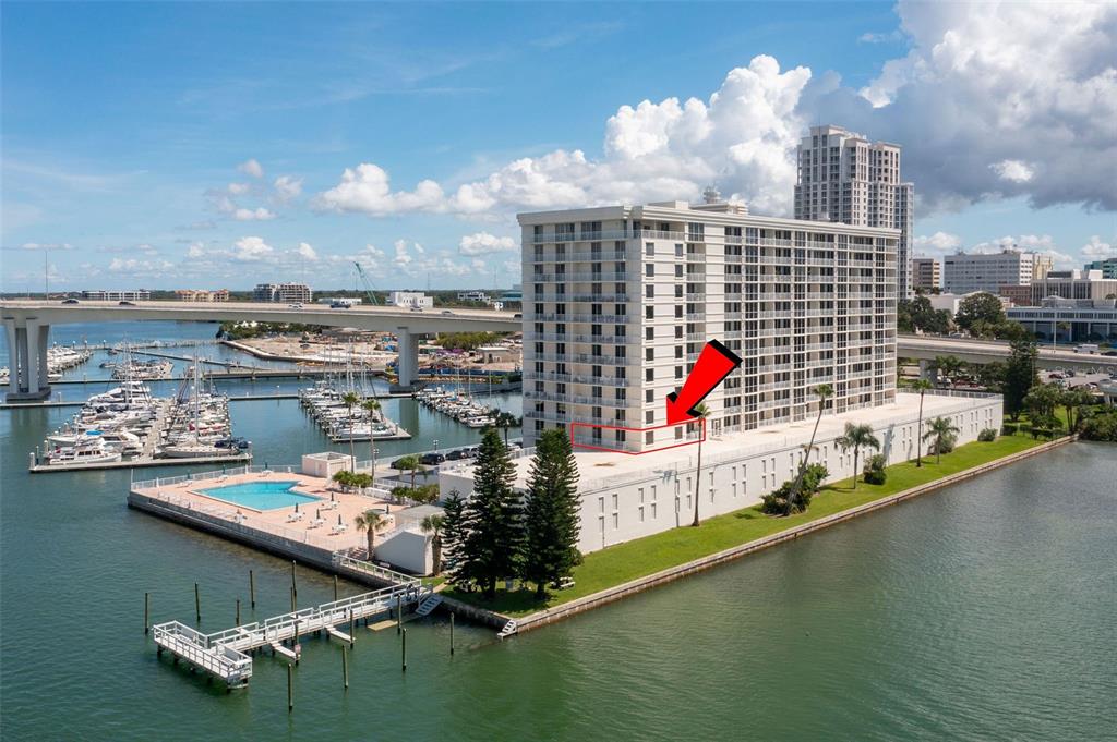 An aerial view shows a high-rise waterfront condominium building with a red arrow pointing to a balcony — 100 PIERCE STREET UNIT 307, CLEARWATER, FL