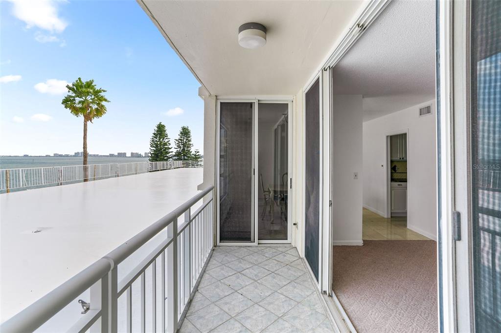 A balcony with light tile flooring overlooks a body of water and a palm tree — 100 PIERCE STREET UNIT 307, CLEARWATER, FL