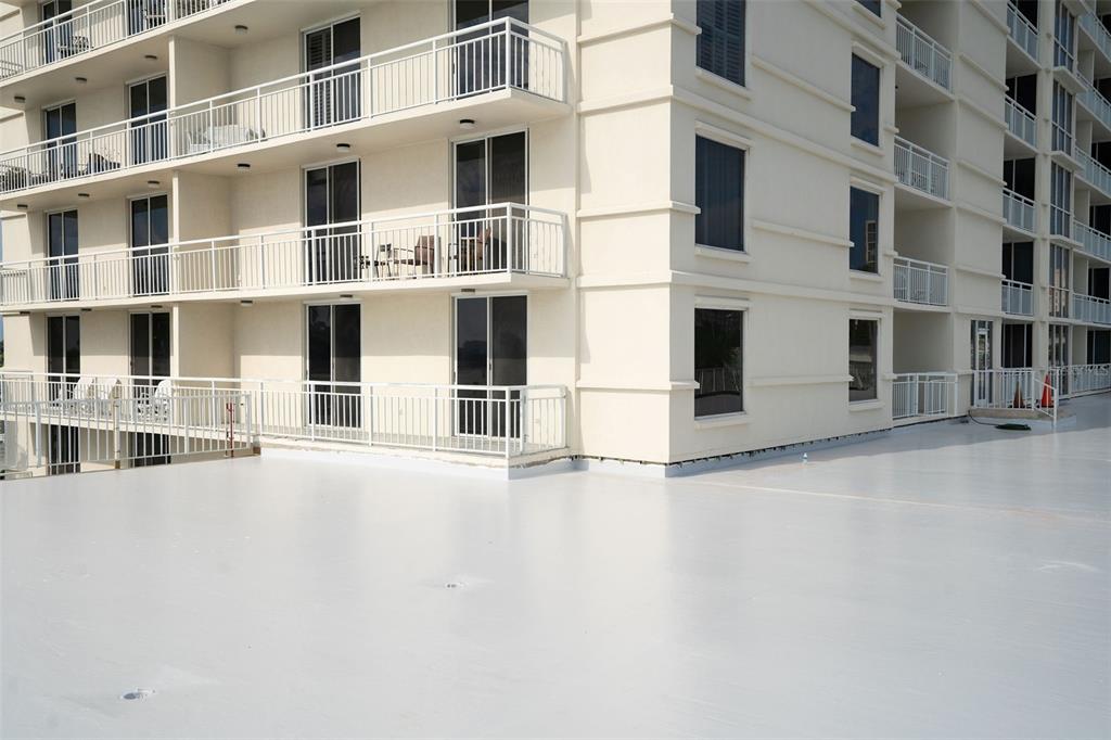 A low-angle view of a multi-story apartment building with a large, flat, light-colored roof terrace — 100 PIERCE STREET UNIT 307, CLEARWATER, FL