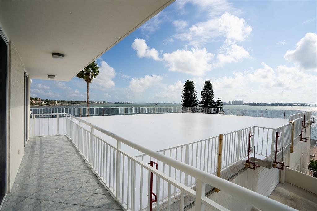 A balcony with tiled flooring overlooks a flat white roof and a coastal bay view — 100 PIERCE STREET UNIT 307, CLEARWATER, FL