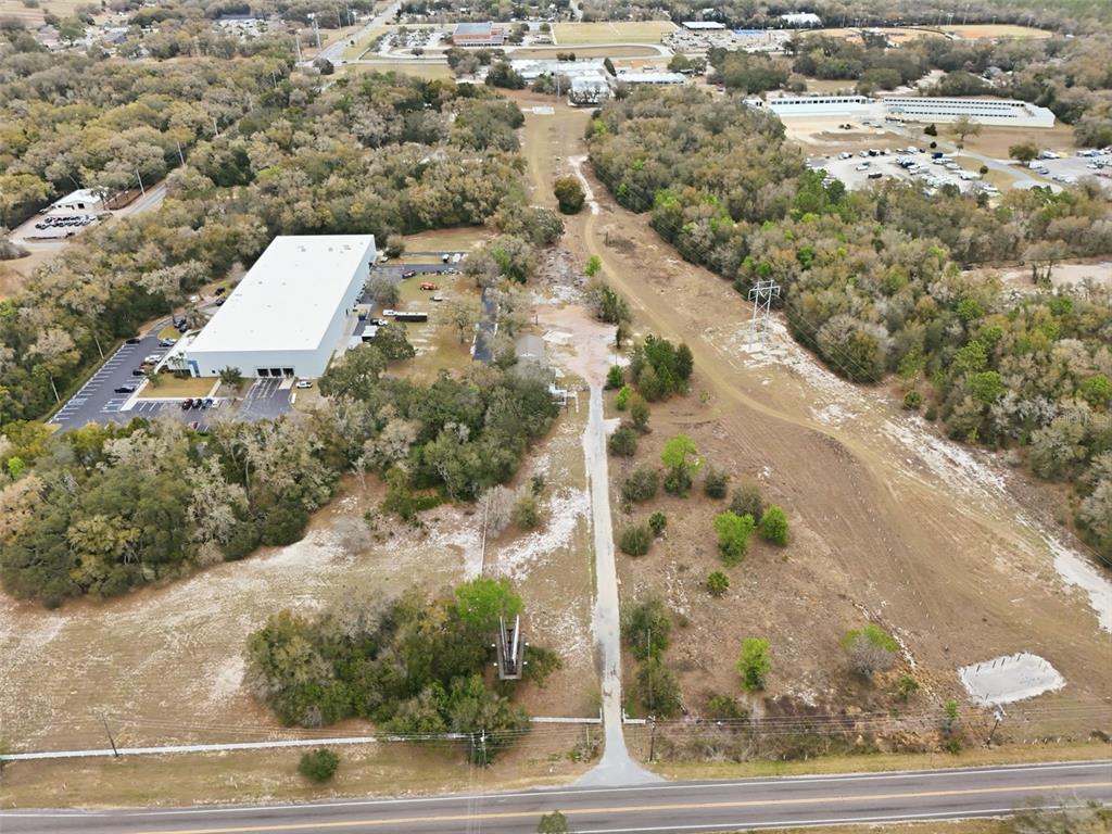 An aerial view shows a large warehouse, a dirt driveway, and surrounding wooded land — 24629 SORRENTO AVENUE, SORRENTO, FL