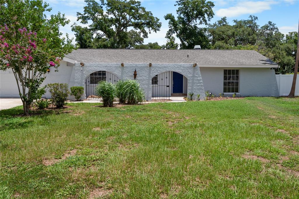 A single-story house with a white stucco facade, arched entryways, and a gray shingled roof — 3104 FAIRLEA LANE, VALRICO, FL