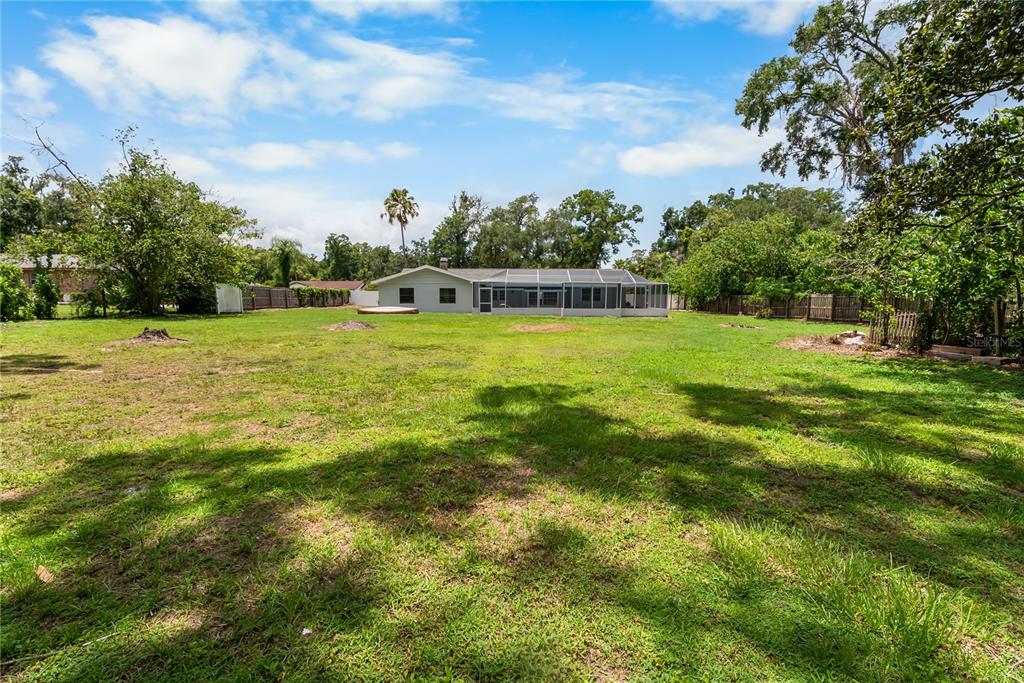 A large, grassy backyard leads to a single-story house with a screened-in pool enclosure — 3104 FAIRLEA LANE, VALRICO, FL