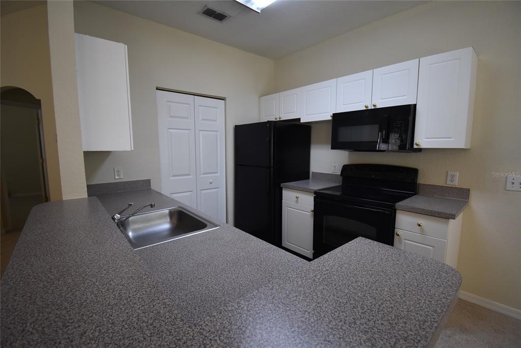 A kitchen features white cabinets, black appliances, and gray speckled countertops with a breakfast bar — 862 GRAND REGENCY POINT UNIT 205, ALTAMONTE SPRINGS, FL
