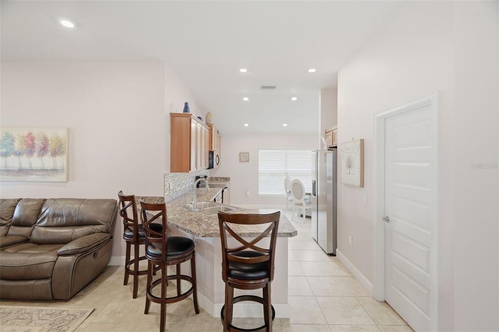 A kitchen with a breakfast bar, wooden cabinets, and tile flooring opens to a living area — 14449 POTTERTON CIRCLE, HUDSON, FL