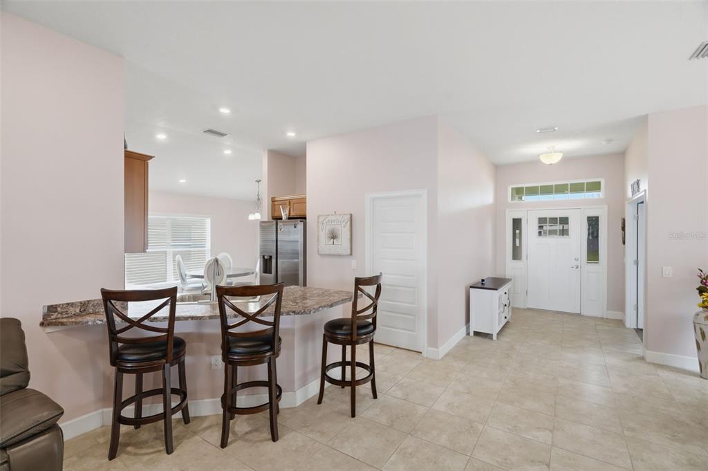 A kitchen with a breakfast bar and stools opens into a light-filled entryway with tile floors — 14449 POTTERTON CIRCLE, HUDSON, FL