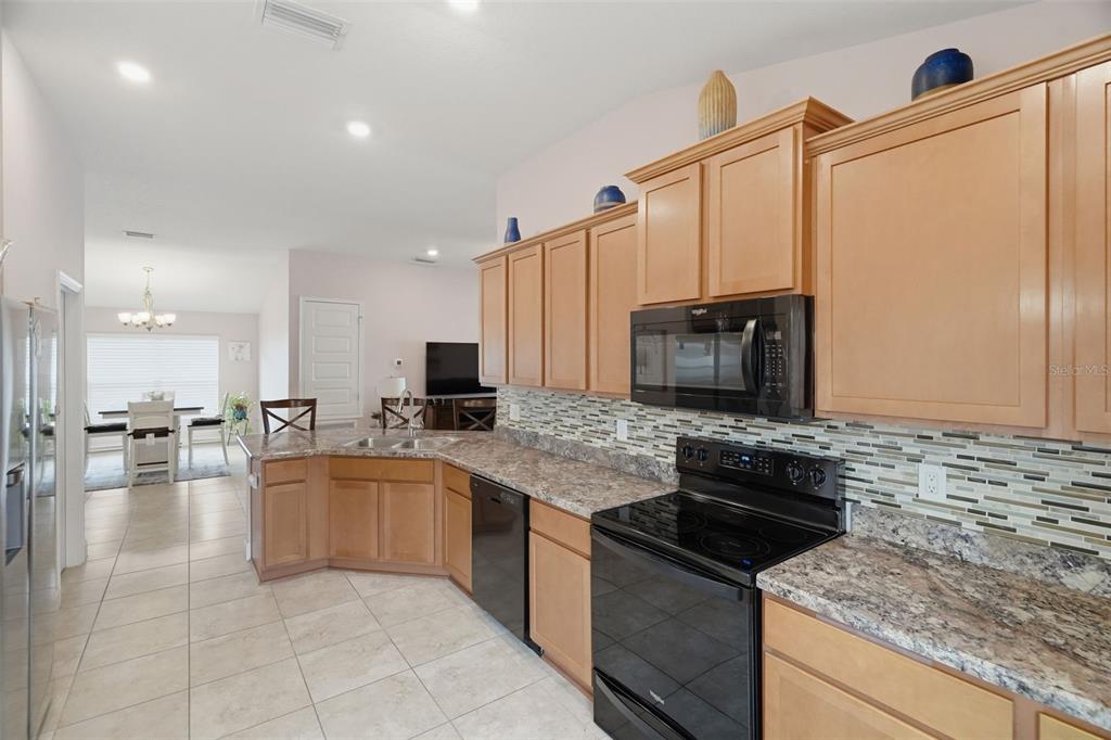 A kitchen features light wood cabinets, granite-look countertops, black appliances, and a tiled backsplash — 14449 POTTERTON CIRCLE, HUDSON, FL
