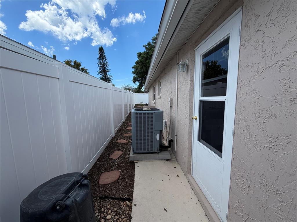 A side exterior view of a house featuring a white fence, HVAC unit, and door — 9135 GREENBRIAR LANE, PORT RICHEY, FL
