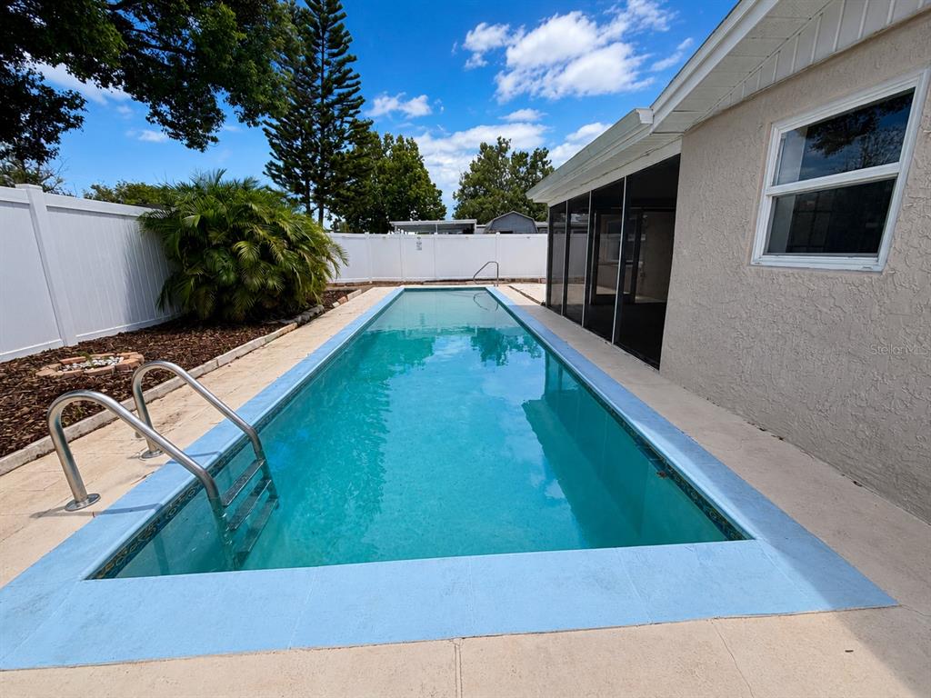 A rectangular swimming pool sits on a patio next to a house with a screened porch — 9135 GREENBRIAR LANE, PORT RICHEY, FL