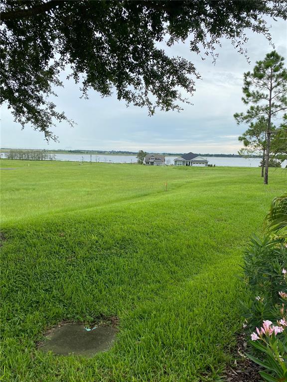 A grassy lot overlooks a lake with two houses in the distance under a cloudy sky — 262 AMARYLLIS WAY, LAKE ALFRED, FL