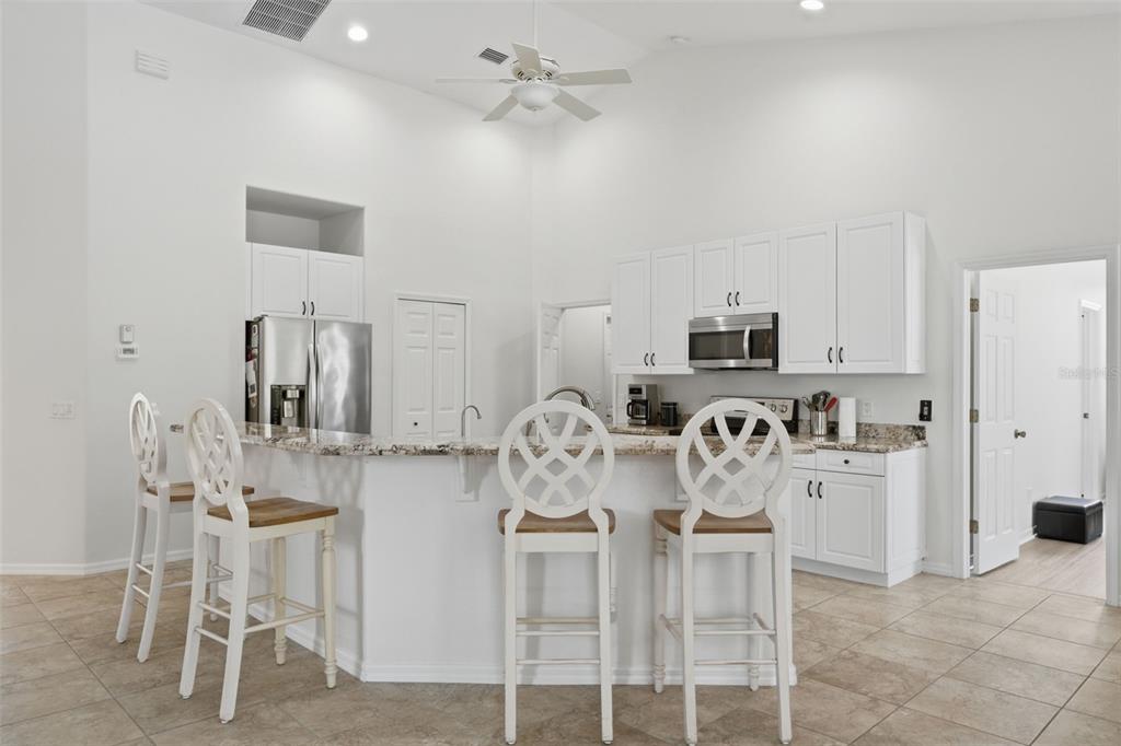 A kitchen with white cabinets, granite countertops, a breakfast bar, and four white wooden chairs — 5936 SW 1ST COURT, CAPE CORAL, FL