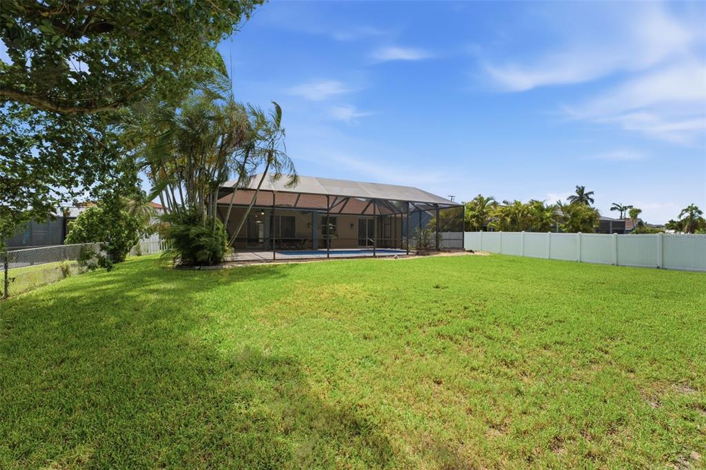 A grassy backyard features a screened-in pool enclosure and a white vinyl privacy fence — 5936 SW 1ST COURT, CAPE CORAL, FL
