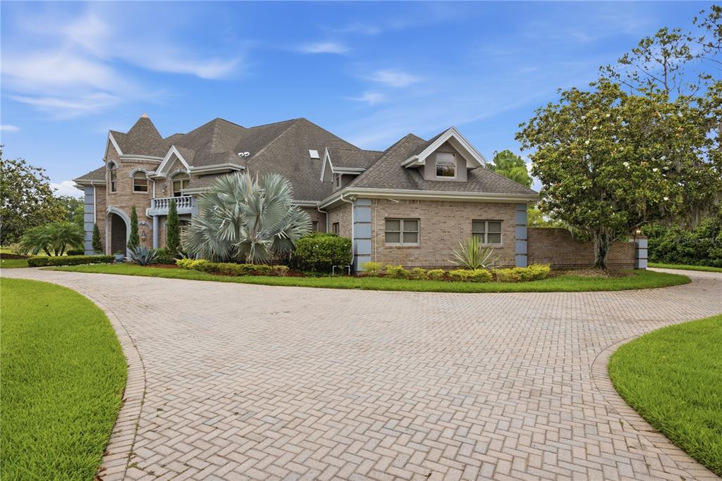 A large brick house with a paved driveway and landscaped yard under a blue sky — 4123 HIGHLAND PARK CIRCLE, LUTZ, FL