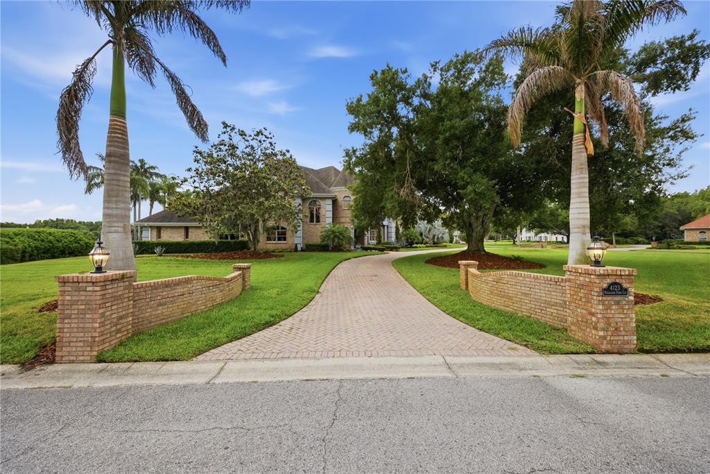 A brick driveway leads to a large house framed by palm trees and mature oaks — 4123 HIGHLAND PARK CIRCLE, LUTZ, FL