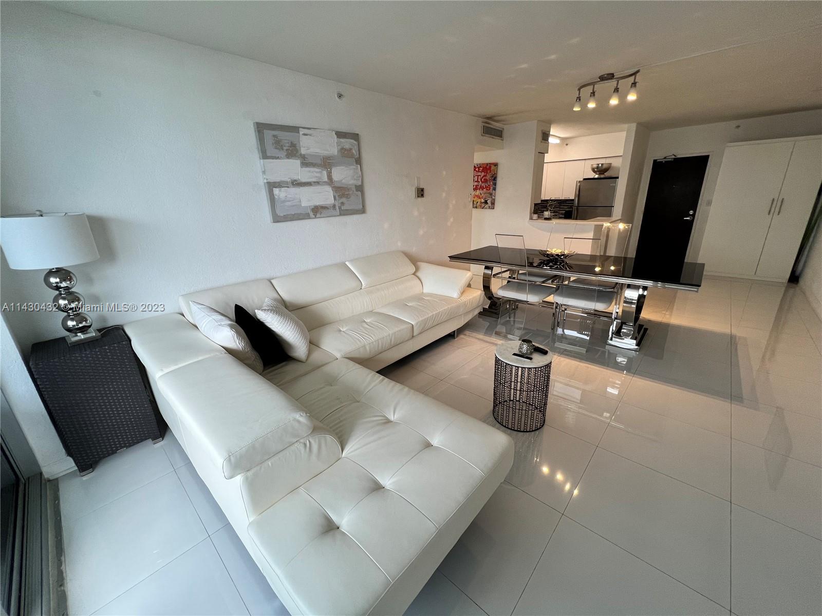 A modern living and dining area features white leather furniture, tile flooring, and a kitchen — 1500 Bay Rd # 1164S, Miami Beach FL 33139, MIAMI BEACH, FL