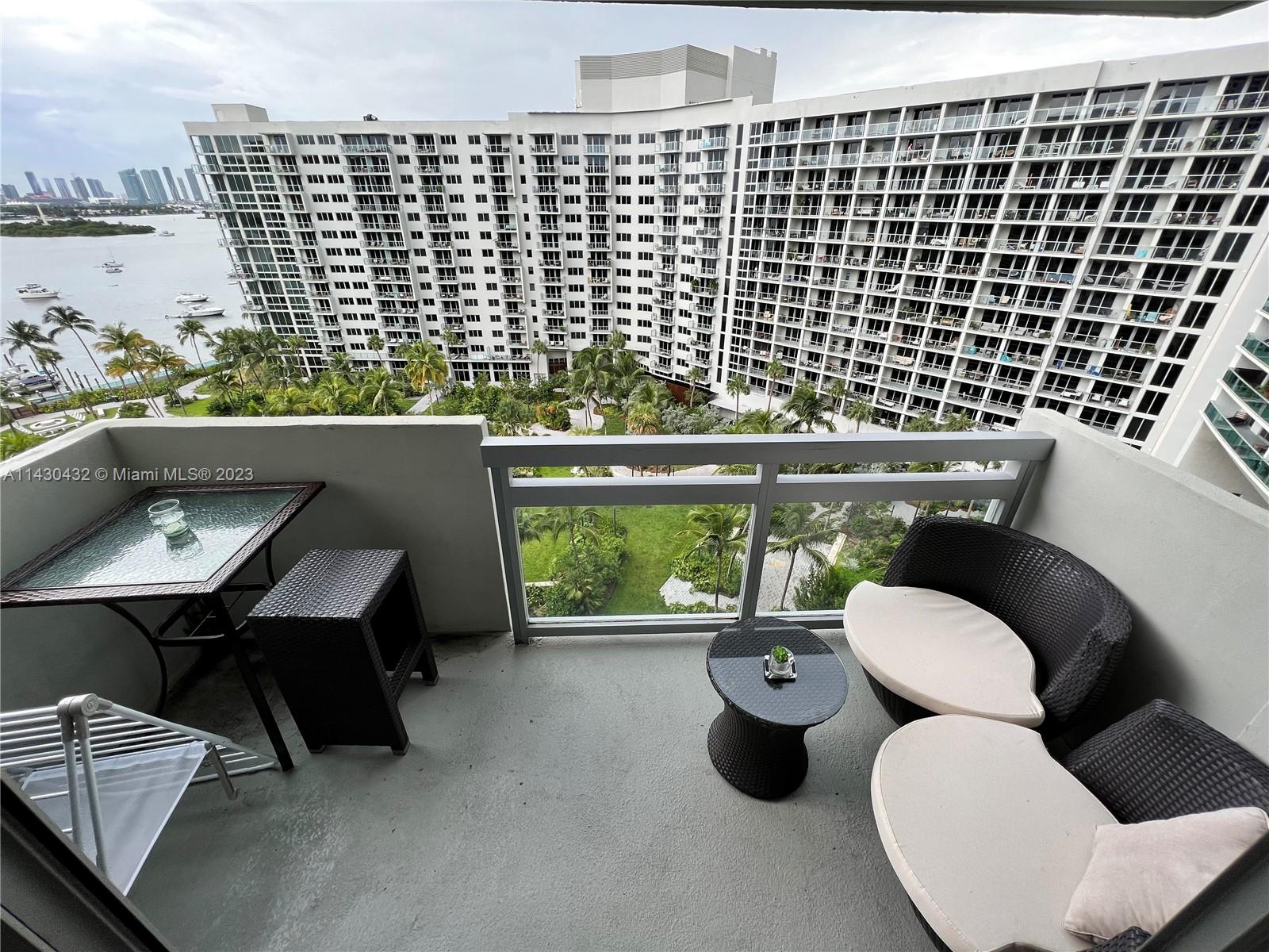 A balcony features outdoor furniture, a glass-topped table, and views of a large apartment complex — 1500 Bay Rd # 1164S, Miami Beach FL 33139, MIAMI BEACH, FL