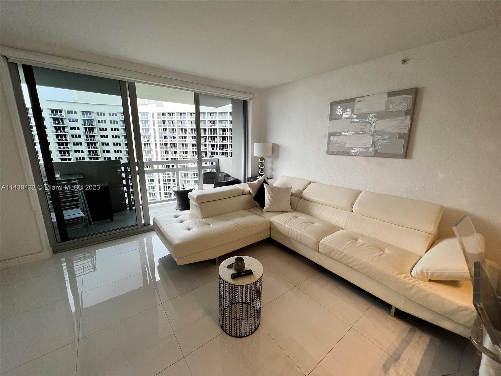 A living room features a white sectional sofa, a small round table, and a balcony view — 1500 Bay Rd # 1164S, Miami Beach FL 33139, MIAMI BEACH, FL