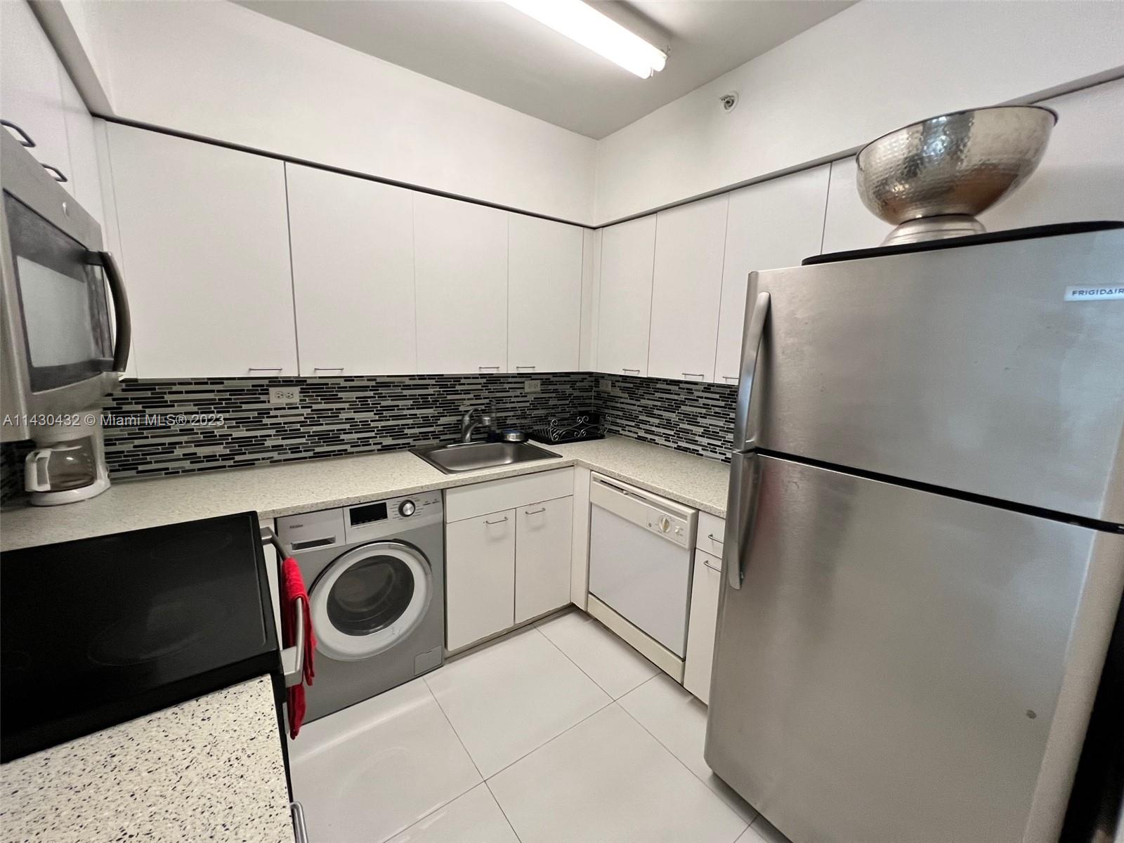 A kitchen features white cabinets, stainless steel appliances, a built-in washer, and a tiled backsplash — 1500 Bay Rd # 1164S, Miami Beach FL 33139, MIAMI BEACH, FL