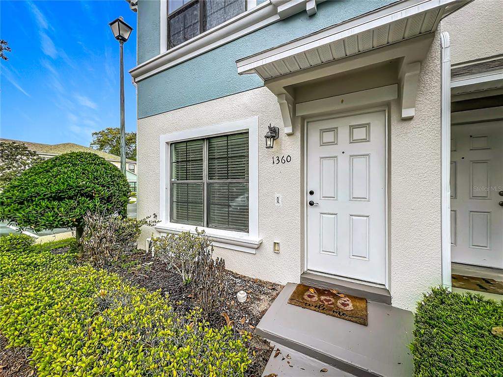 The exterior of a residential building features a white front door, a window, and landscaping — 1360 WINDSOR LAKE CIRCLE, SANFORD, FL
