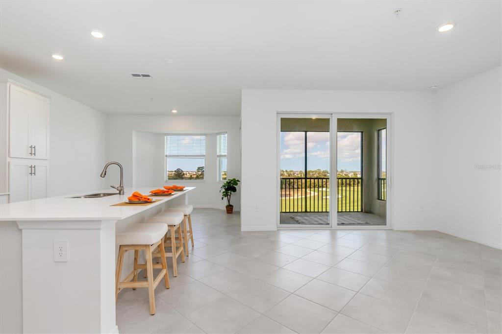 A bright kitchen with a white island and stools overlooks a patio with golf course views — 17595 OPAL SAND DRIVE UNIT 406, VENICE, FL