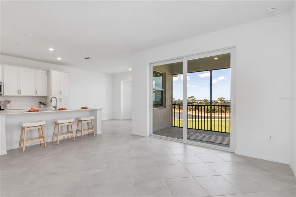 A bright kitchen with white cabinets and a breakfast bar opens to a screened patio — 17595 OPAL SAND DRIVE UNIT 406, VENICE, FL