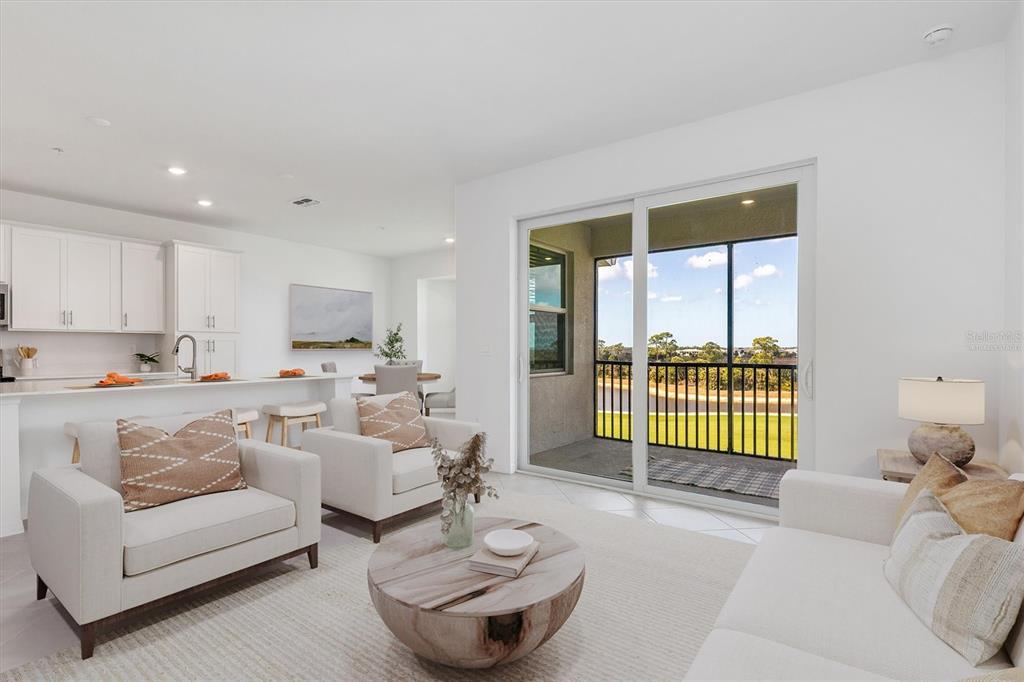 A bright living room features white furniture, a round wooden coffee table, and a balcony — 17595 OPAL SAND DRIVE UNIT 406, VENICE, FL