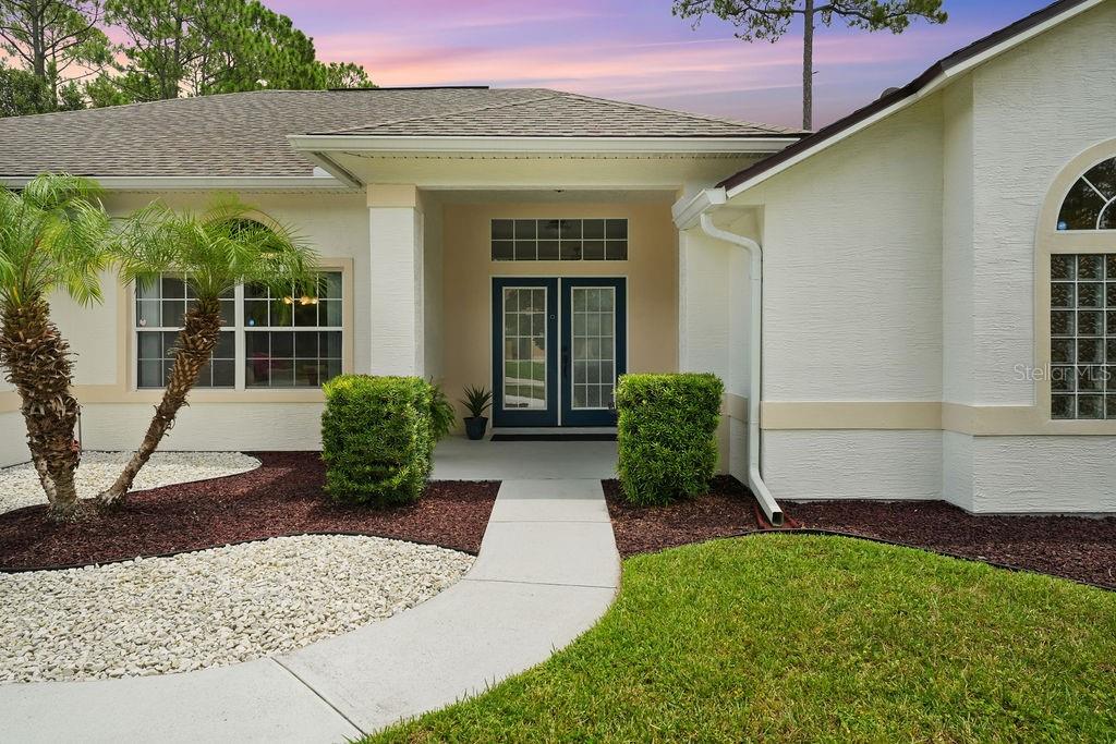 The exterior of a house features a white stucco facade, a covered entryway, and landscaping — 58 RYBERRY DRIVE, PALM COAST, FL