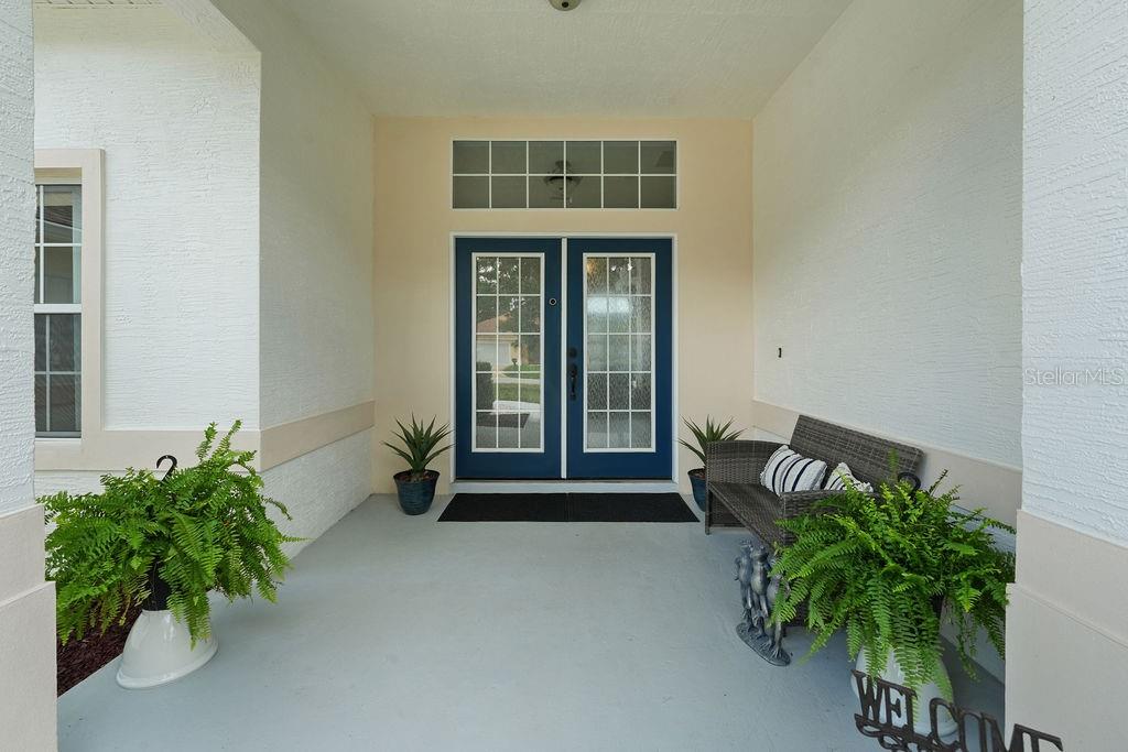 A covered front porch features a double door entrance, a bench, and potted ferns — 58 RYBERRY DRIVE, PALM COAST, FL
