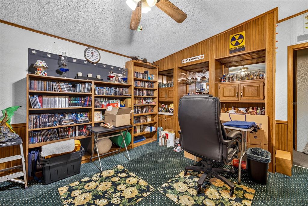 A home office features wood-paneled walls, built-in shelving, a ceiling fan, and green patterned carpeting — 16435 SWEETWATER ROAD, DADE CITY, FL