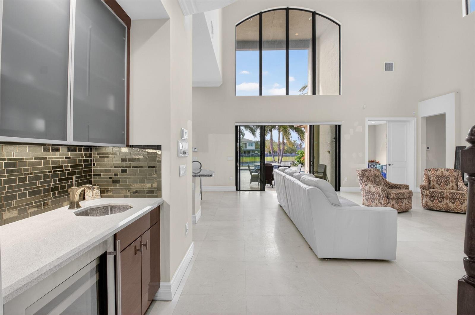 A wet bar with a tiled backsplash overlooks a living room with high ceilings — 16801 Pavilion Way, Delray Beach FL 33446, DELRAY BEACH, FL