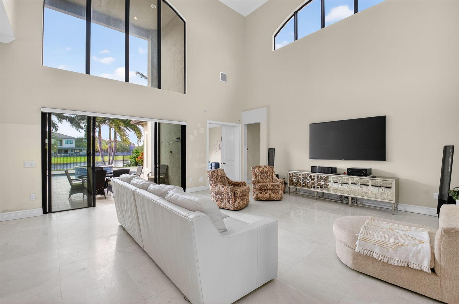 A spacious living room features high ceilings, tile floors, a large television, and patio access — 16801 Pavilion Way, Delray Beach FL 33446, DELRAY BEACH, FL