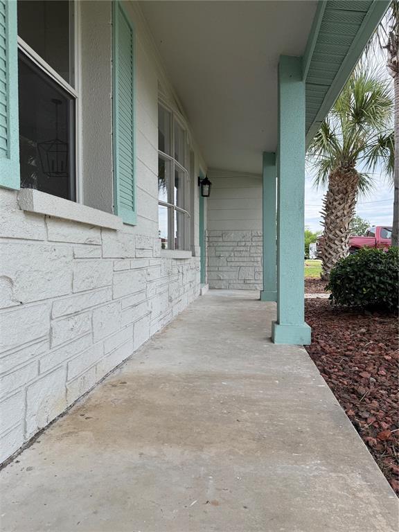 A covered concrete porch features light-colored stone siding, teal-painted columns, and matching window shutters — 13423 SUSAN DRIVE, HUDSON, FL