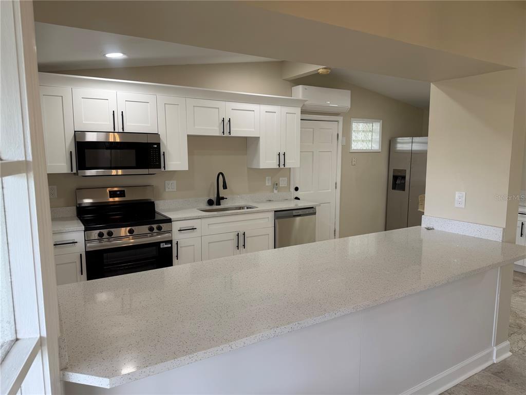 A kitchen features white cabinets, stainless steel appliances, and a light-colored quartz countertop island — 13423 SUSAN DRIVE, HUDSON, FL
