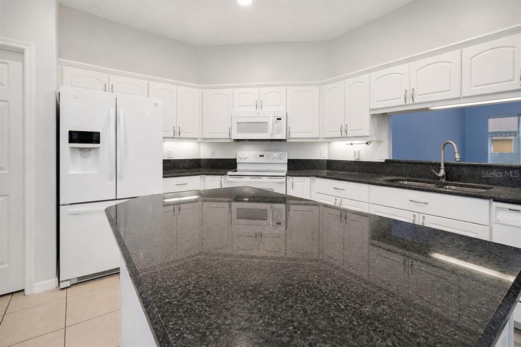 A kitchen features white cabinets, dark granite countertops, a large island, and white appliances — 26903 HONEYMOON AVENUE, LEESBURG, FL