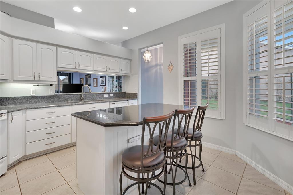 A kitchen features white cabinets, granite countertops, a central island with three stools, and shutters — 26903 HONEYMOON AVENUE, LEESBURG, FL