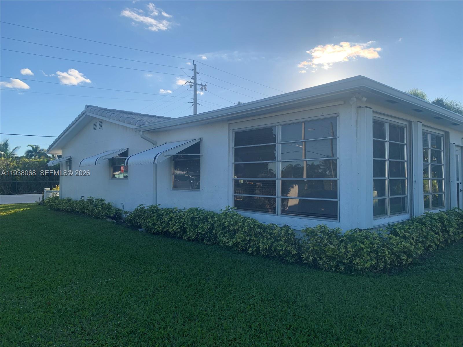 A white, single-story house features louvered windows, metal awnings, and a manicured hedge — 1801 SW 22nd Way, Boynton Beach FL 33426, BOYNTON BEACH, FL