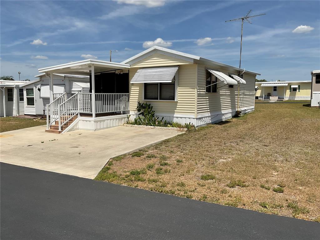A light yellow mobile home with a covered front porch and concrete driveway — 38130 MCDONALD STREET UNIT 23, DADE CITY, FL