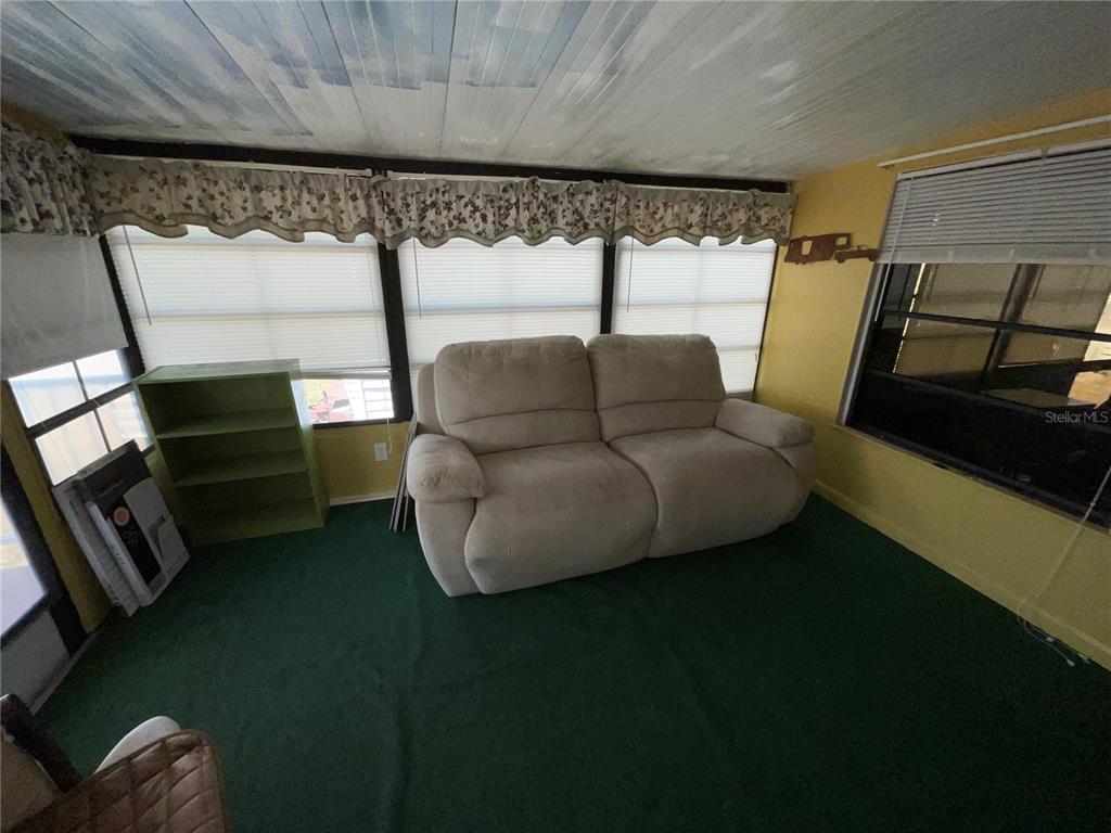 A sunroom features green carpeting, a light-colored loveseat, and windows with pleated shades — 38130 MCDONALD STREET UNIT 23, DADE CITY, FL