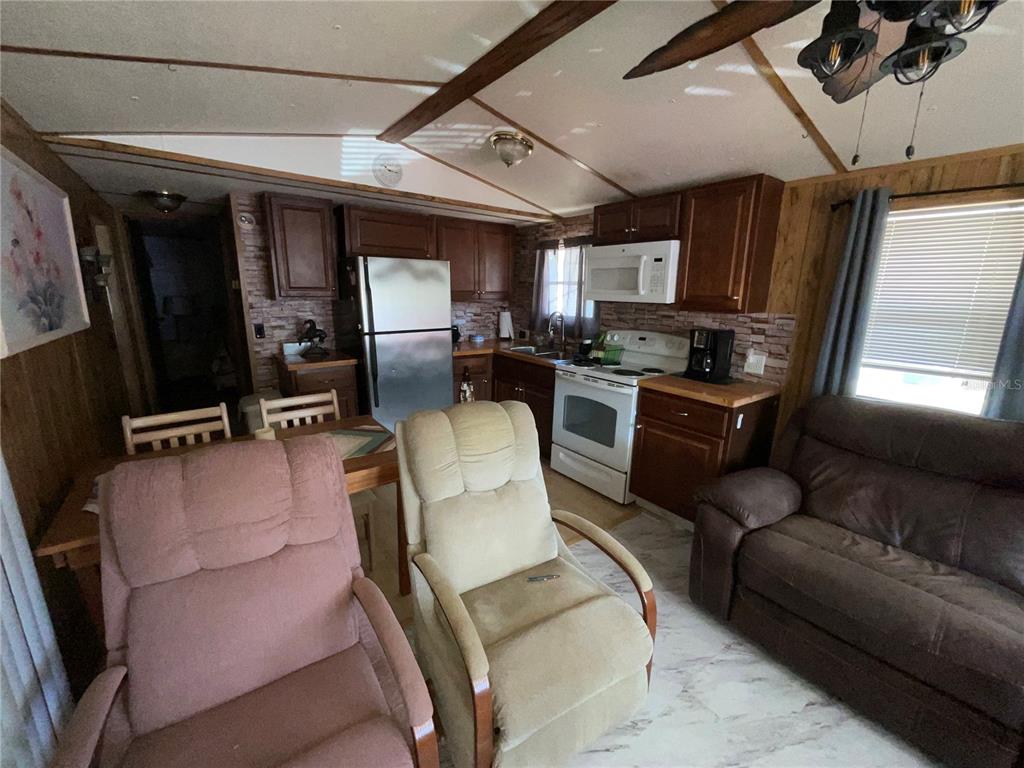 A kitchen and living area featuring wood cabinets, stainless steel appliances, and two recliner chairs — 38130 MCDONALD STREET UNIT 23, DADE CITY, FL