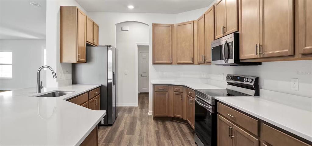 A kitchen features light wood cabinets, white countertops, stainless steel appliances, and wood-look flooring — 1161 TIMBERWOOD DRIVE, WILDWOOD, FL