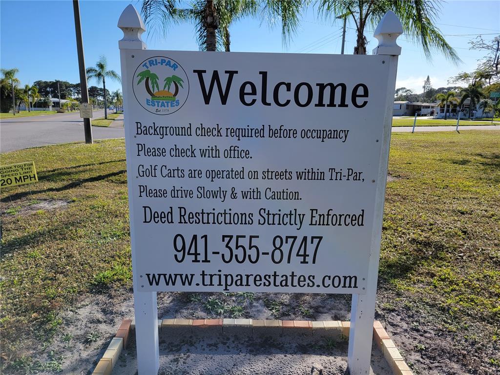 A white welcome sign for Tri-Par Estates stands in a grassy area with palm trees — 5254 PEBBLE BEACH AVENUE, SARASOTA, FL