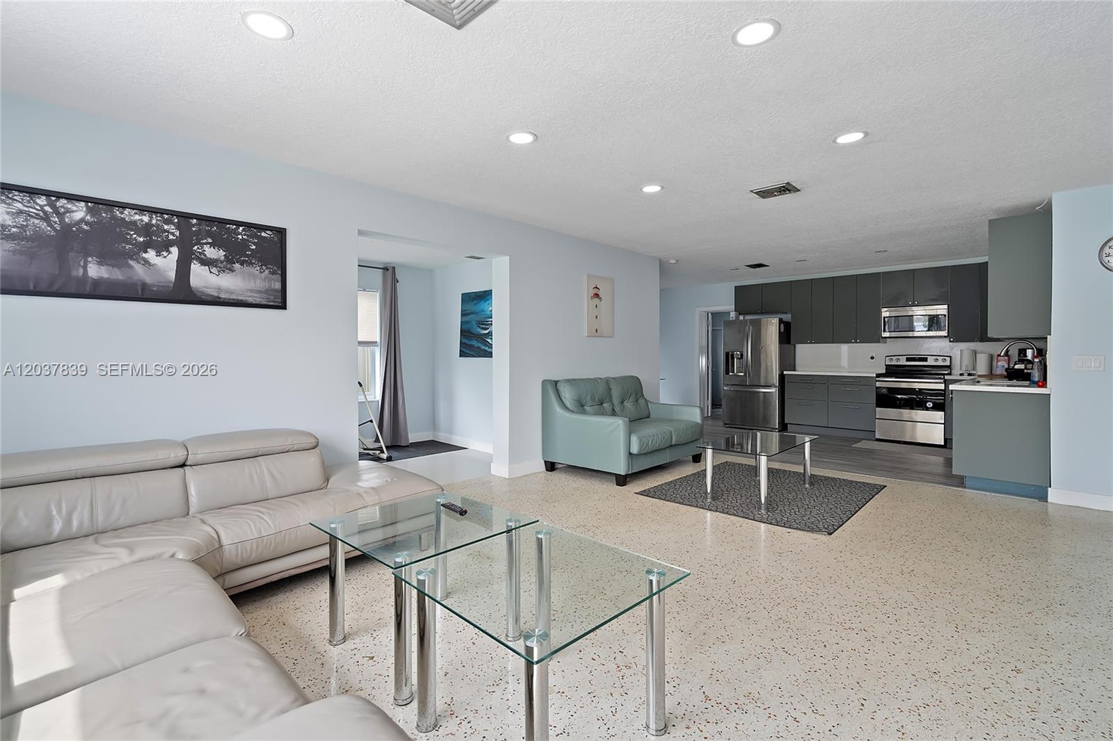 An open-concept living room and kitchen feature light-colored walls, terrazzo flooring, and gray cabinetry — 644 SW 7th Ct # 0, Hallandale Beach FL 33009, HALLANDALE BEACH, FL