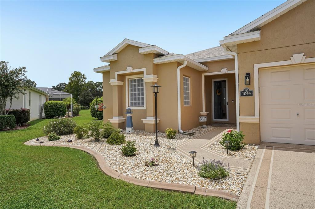 A tan single-story house with a gravel front yard, a concrete walkway, and a garage — 1044 SW 159TH STREET, OCALA, FL