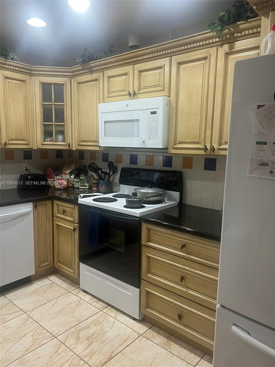 A kitchen features light wood cabinets, black countertops, a white stove, and tiled flooring — 176 Cape Cod Circle # 0, Lake Worth FL 33467, LAKE WORTH, FL